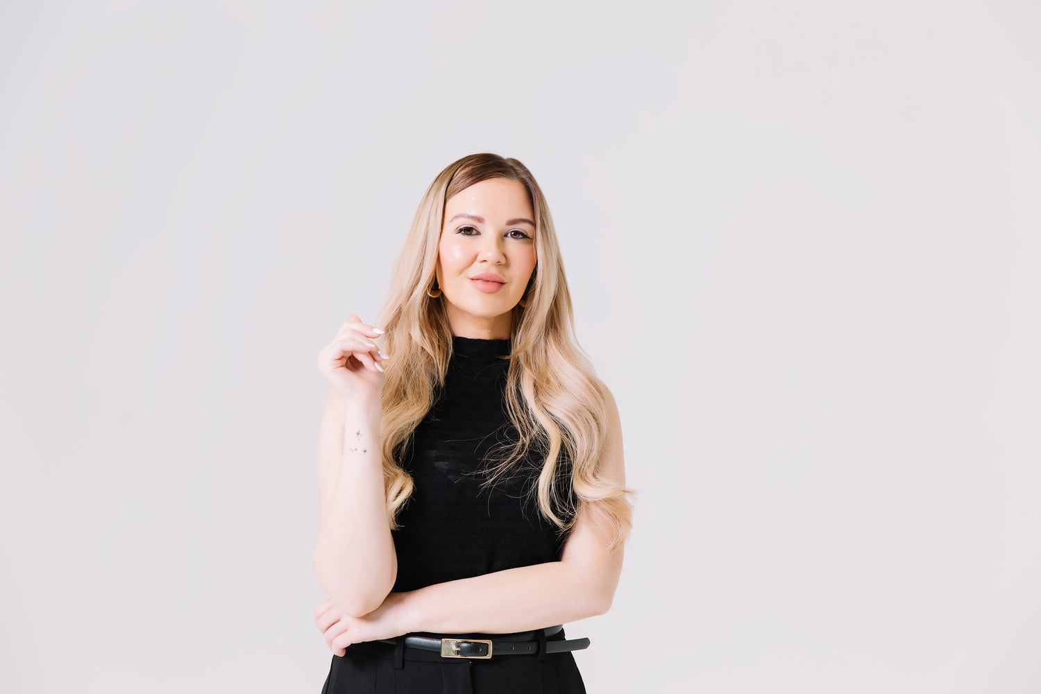 Woman with long blonde hair wearing a black top against a light gray background