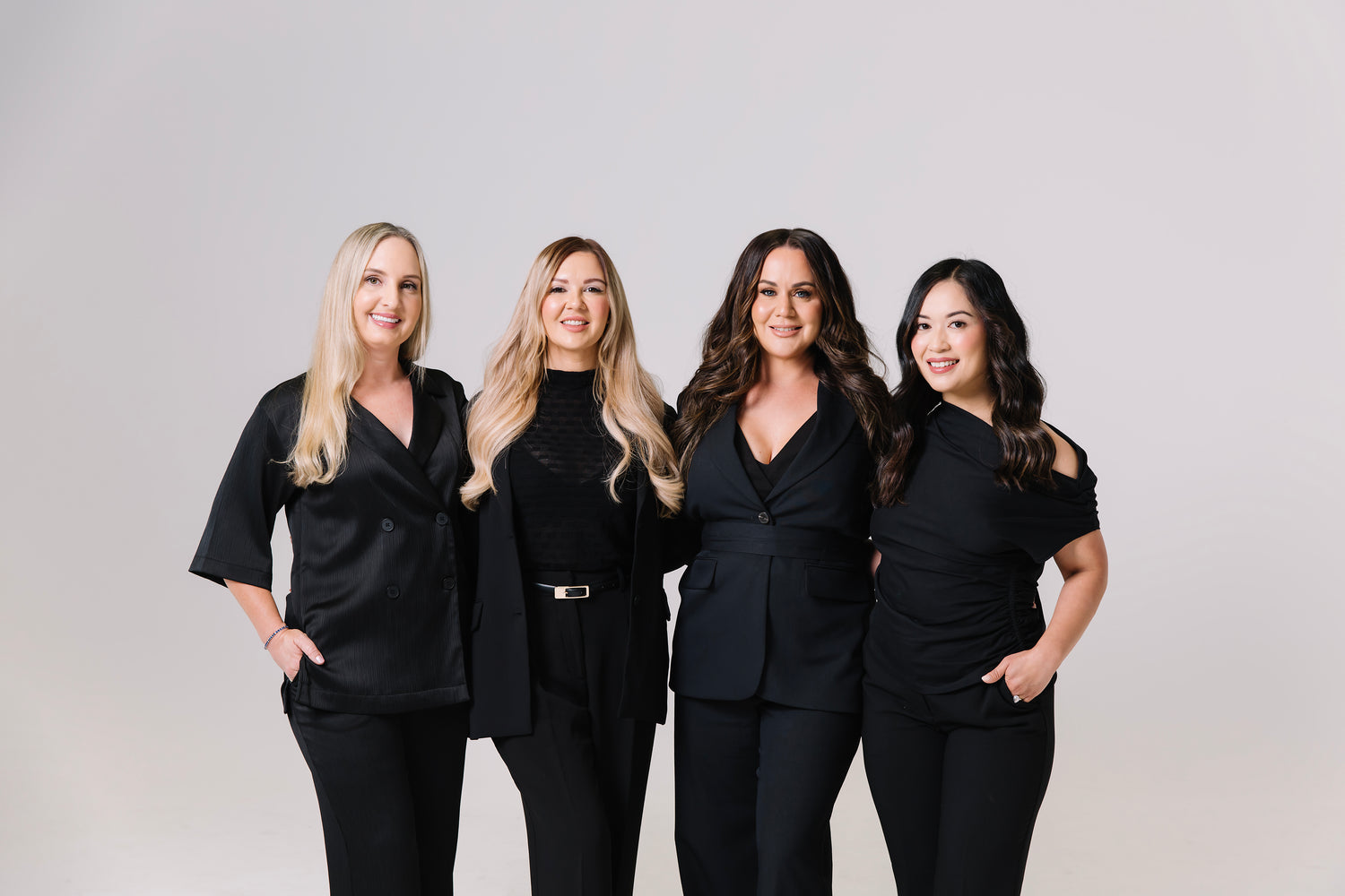 Four cosmetic nurses in black outfits posing together against a plain background